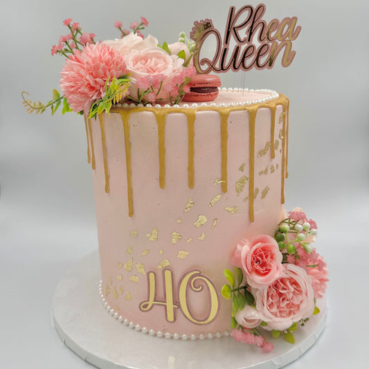 Elegant pink and gold 40th birthday cake with gold drip, edible gold leaf, fresh floral decorations, and a custom pink and gold topper.